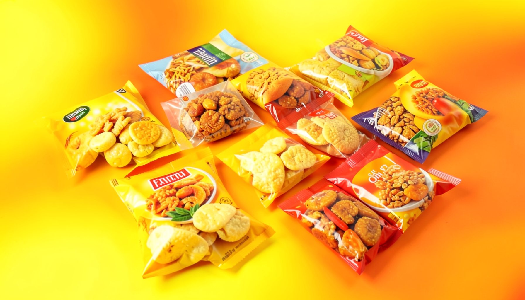 A colorful assortment of packaged Indonesian snacks spread across a bright surface, with warm yellow and orange tones dominating the scene.